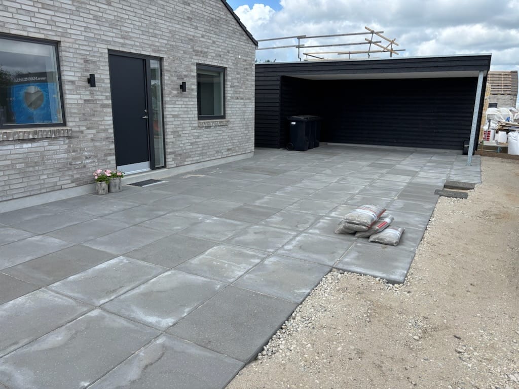 Ny belægning foran moderne murstenshus med carport